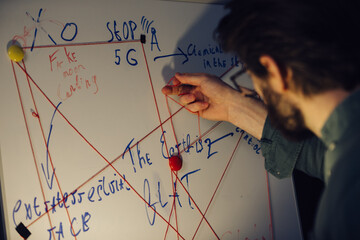 A man is standing near a crazy table on a conspiracy theory board.