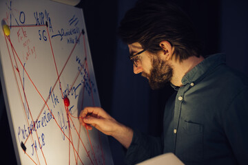 A man is standing near a crazy table on a conspiracy theory board.