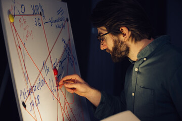 A man is standing near a crazy table on a conspiracy theory board.