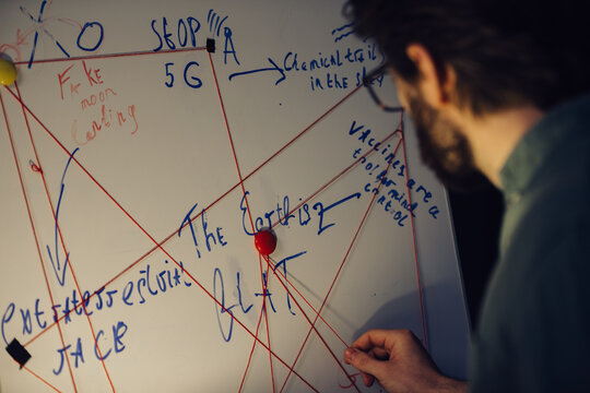 A man is standing near a crazy table on a conspiracy theory board.