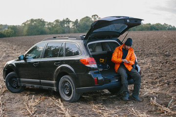 A male archaeologist sits in the trunk of a car holding ancient coins found with a metal detector.