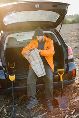 A young man uses an old map to search for treasures with a metal detector.