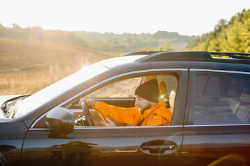 A young man dressed in an orange jacket and cap, in a car with a phone in his hands.