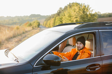 Naklejka premium A young man dressed in an orange jacket and cap, in a car with a phone in his hands.