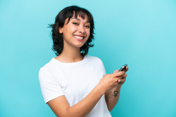 Young Argentinian woman isolated on blue background sending a message or email with the mobile