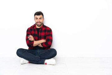 Young handsome man sitting on the floor keeping the arms crossed in frontal position