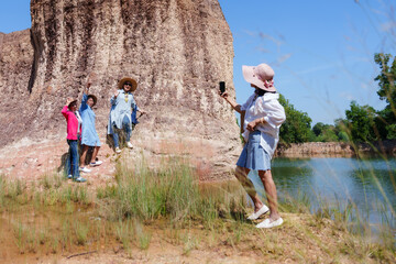 Four elderly Asian women, dressed casually, pose by a rock formation, waving and smiling while enjoying their outdoor adventure. Clear skies and warm sunlight add to the lively, joyful moment.