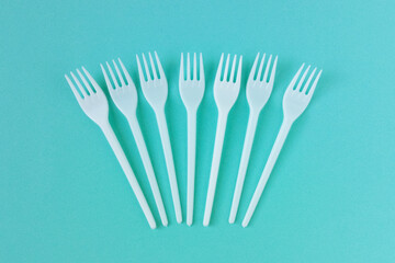 Seven white plastic forks on a turquoise background. Top view.