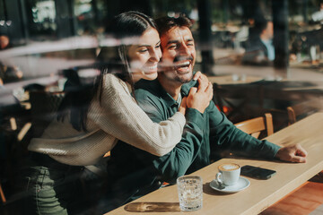 Couple enjoying a warm afternoon together in a cozy cafe, sharing smiles and laughter over coffee while seated by a large window