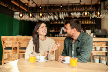 Couple enjoying at a cozy cafe with warm drinks and laughter in a vibrant, modern setting on a sunny afternoon