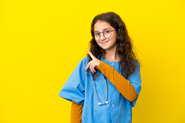Little nurse girl isolated on yellow background pointing to the side to present a product