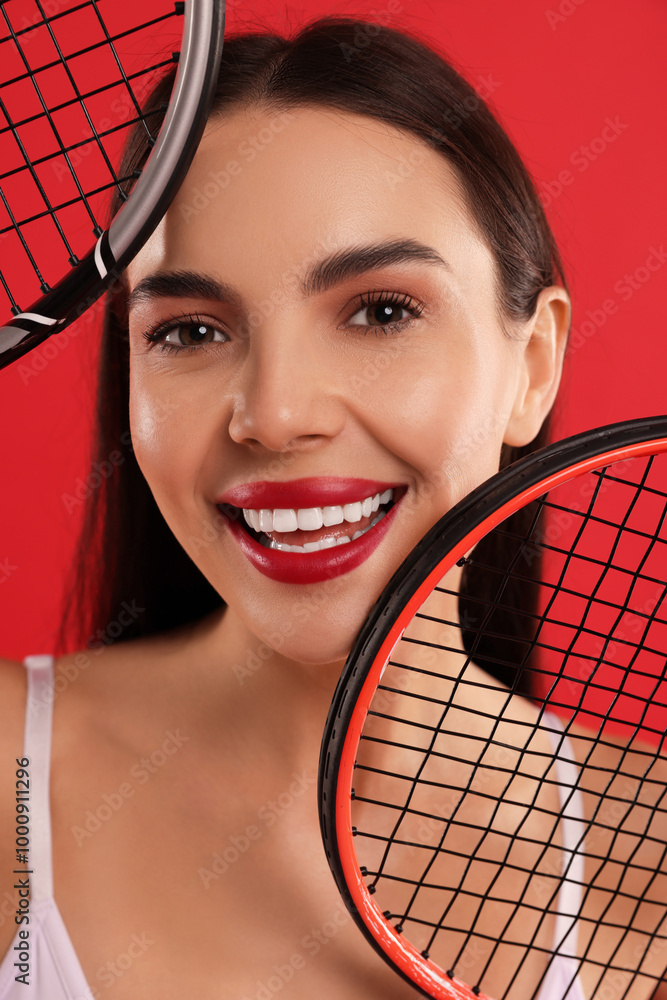 Poster Portrait of beautiful young woman with tennis rackets on red background, closeup