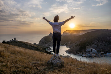 Happy woman on sunset in mountains. Woman standing with her back on the sunset in nature in summer with open hands. Silhouette.