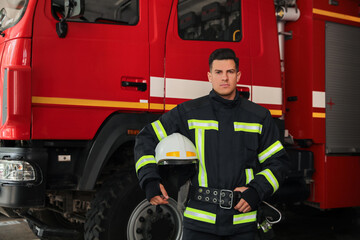 Portrait of firefighter in uniform with helmet near fire truck at station, space for text