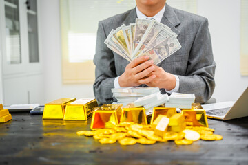 Businessman in suit sits at his desk, holding a shining gold bar. financial charts, the scene...