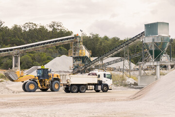 Loader and tipper truck at a quarry site with machinery in background