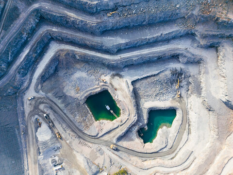 Aerial view looking down into a tiered quarry pit with machinery and water ponds