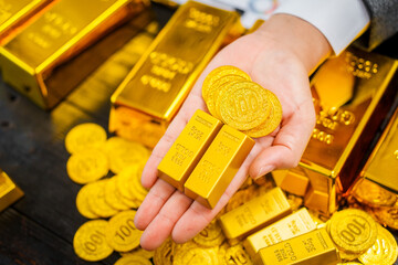 Businessman in suit sits at his desk, holding a shining gold bar. financial charts, the scene...