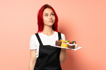 Pastry chef holding a muffins isolated on pink background and looking up