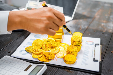 Businessman in suit sits at his desk, holding a shining gold bar. financial charts, the scene...