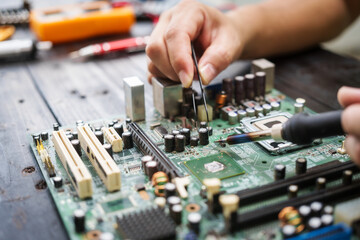 Technician carefully repairs a computer circuit board, using precision tools to address hardware issues. technical expertise needed for troubleshooting and upgrading electronic systems in workspace.