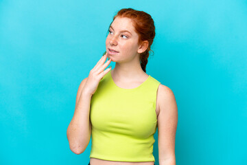 Young reddish woman isolated on blue background looking up while smiling