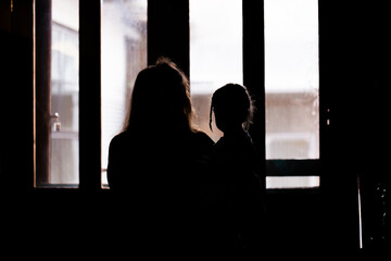 Silhouette of woman holding young child looking out window on rainy day