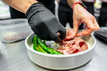 A close-up of hands in black gloves preparing a fresh meal with green vegetables and raw meat in a bowl. The scene captures the precision and care in culinary preparation