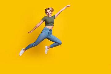 Obraz premium Full size photo of lovely positive girl dressed khaki crop top jeans fly to empty space raising fist isolated on yellow color background