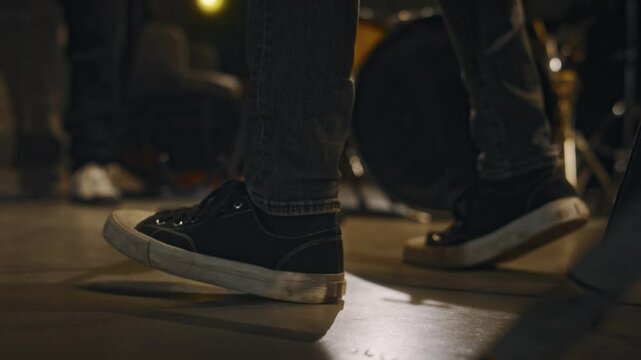 Close-up of feet of unrecognizable man wearing canvas shoes tapping in time to music while spending time with bandmates at recording studio