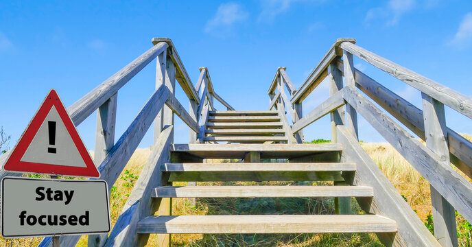 Sign Stay focused in front of wooden Stairs up to blue sky