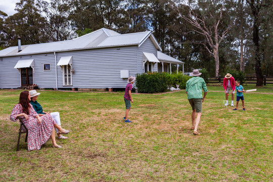 Australian family playing backyard cricket with mum and grandma watching the game - Powered by Adobe