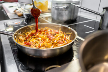 Stir-fried noodles with vegetables and tomato sauce in pan, steam rising, kitchen background. Perfect for food blogs, recipe websites, or culinary magazines. Vibrant colors and appetizing presentation