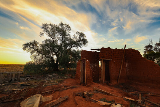 Ruins of abandoned mud brick home on rural property at sunset