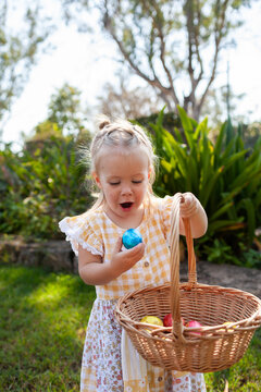 Happy toddler doing an easter egg hunt in garden finding chocolate egg