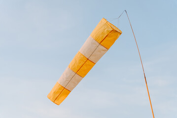 Wind meter at blue sky at sunset, yellow and white cone-shaped windsock
