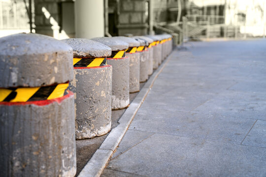 series of large concrete bollards marked with yellow-black tape, symbolizing urban safety and delineation of spaces while emphasizing contrast between industrial materials and safety measures - Powered by Adobe