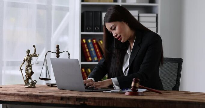 Business woman or lawyer works in the office or court, checks clients contracts, calling by phone. Asian successful business lady, statuette of Themis, goddess of justice. legal advice online.
