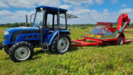 Obraz premium A blue tractor towing bright red agricultural machinery across a green field on a sunny day. The scene captures the essence of modern farming with vibrant colors and expansive rural landscape