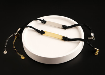 Jewelry for women. Gold and silver bracelets on a cord with a pendant on a black background. White stand for jewelry.