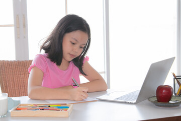 Adorable Asian girl happy learning online with technology laptop on desk at home, school girl typing answer or response with teacher study homeschool or learn from home, smart kids with technology