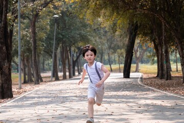 Young Asian boy running energetically down a tree-lined path in a park, capturing a playful and active moment outdoors. carefree expression reflects excitement and freedom to enjoy fresh air outdoor