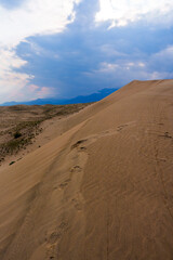 Expansive desert dunes stretch under a dramatic sky with sunbeams breaking through the clouds, creating a serene and awe-inspiring landscape. 