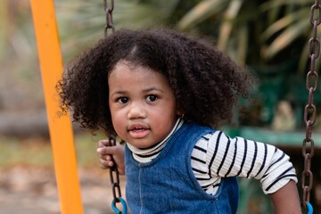 Young Afro hair elementary schoolgirl crawling through colorful tunnel on a playground, weekend carefree holiday in park. bright playground equipment and focus expression capture childhood exploration