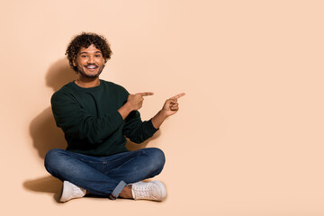 Full size photo of nice young man indicate fingers empty space wear sweater isolated on beige color background