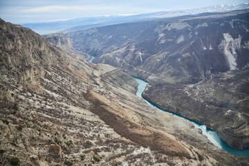 A blue river flows through the canyon. The landscape is dry, without any vegetation, the season is winter. The water is calm and peaceful.