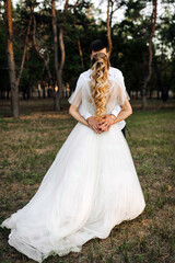 Fototapeta premium Groom hugging curly blonde bride from behind outdoors in forest. Wedding photography.