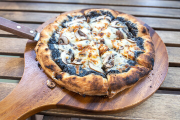 Truffle Champignon mushroom Pizza in round wooden tray serving with handle on a slatted table in a cafe restaurant.