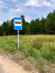 A bus stop sign stands on the side of a quiet rural road, surrounded by grassy fields and a...