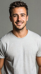 Fototapeta premium Portrait of a young man with short brown hair and a beard wearing a grey t-shirt, smiling on a grey background